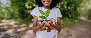 Girl in white tshirt with cupped hands holding a green shoot